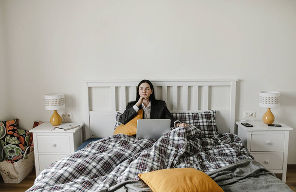 businesswoman in pajamas and jacket works at a computer in her checkered bed, bedroom interior design - Zdjęcie, obraz