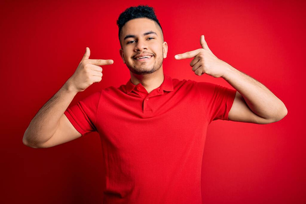 Young handsome man wearing red casual polo standing over isolated background smiling cheerful showing and pointing with fingers teeth and mouth. Dental health concept. - Fotoğraf, Görsel