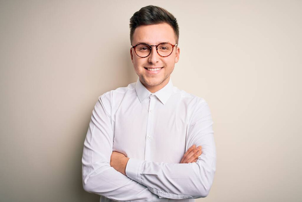 Young handsome business mas wearing glasses and elegant shirt over isolated background happy face smiling with crossed arms looking at the camera. Positive person. - Foto, immagini
