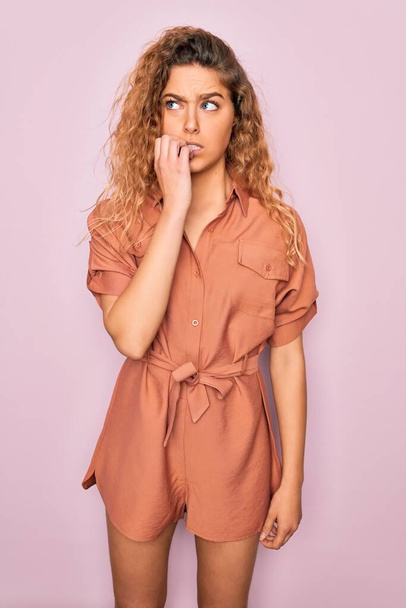 Young beautiful woman with blue eyes wearing casual summer dress over pink background looking stressed and nervous with hands on mouth biting nails. Anxiety problem. - Zdjęcie, obraz