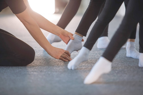 Dłonie trenera pomagają i wspierają stopy w rzędzie stóp nastoletnich dziewcząt w czarnych rajstopach i białych skarpetkach w lekcjach tańca, choreografii, baletu czy gimnastyki rytmicznej. Wybrane skupienie. - Zdjęcie, obraz