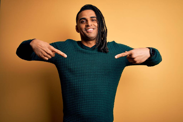 Νεαρός όμορφος αφροαμερικάνος με κοτσιδάκια που φοράει πράσινο casual πουλόβερ που δείχνει σίγουρος με χαμόγελο στο πρόσωπο, δείχνοντας τον εαυτό του με τα δάχτυλα περήφανος και χαρούμενος. - Φωτογραφία, εικόνα