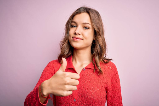 Young beautiful blonde casual girl over pink isolated background doing happy thumbs up gesture with hand. Approving expression looking at the camera showing success. - Foto, imagen