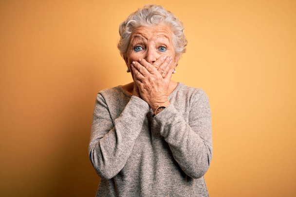 Senior beautiful woman wearing casual t-shirt standing over isolated yellow background shocked covering mouth with hands for mistake. Secret concept. - Foto, Imagem