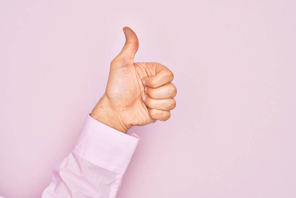 Hand van Kaukasische jongeman met vingers over geïsoleerde roze achtergrond met succesvol goedkeuringsgebaar met duimen omhoog, validatie en positief symbool - Foto, afbeelding