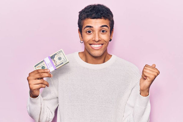 Fiatal afro-amerikai férfi kezében dollár sikoltozik büszke, ünnepli győzelem és a siker nagyon izgatott felemelt karral  - Fotó, kép