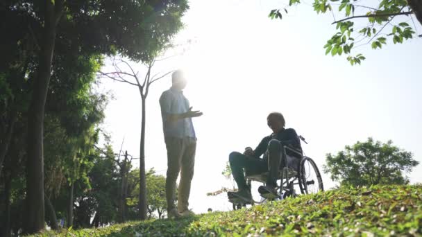 Ασιάτης ενήλικος γιος και πατέρας δεμένος με αναπηρική καρέκλα μιλώντας σε εξωτερικούς χώρους  - Πλάνα, βίντεο