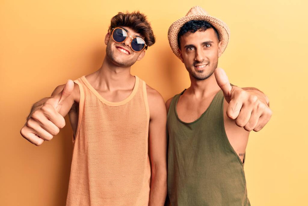 Mladý gay pár v letních šatech, který schvaluje pozitivní gesto rukou, palec nahoru, usmívá se a je šťastný za úspěch. gesto vítěze.  - Fotografie, Obrázek