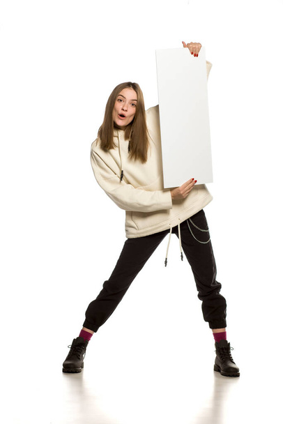 Jovem modelo feliz com capuz segurando uma placa de publicidade vazia no fundo branco
 - Foto, Imagem