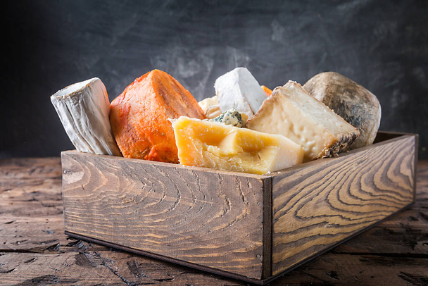 verschillende soorten kaas in houten doos op rustieke houten tafel - Foto, afbeelding