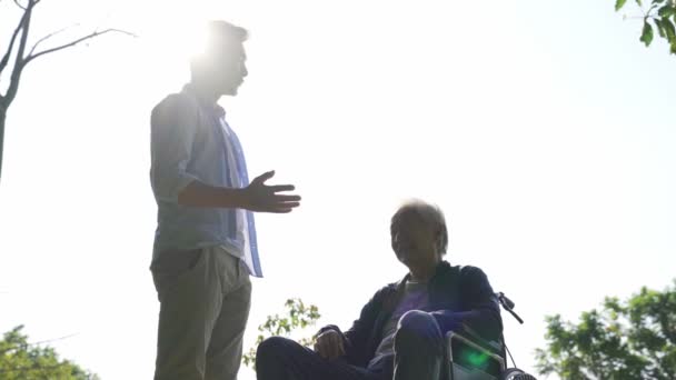 asiático adulto hijo y silla de ruedas obligado padre mayor hablando chat al aire libre
  - Imágenes, Vídeo