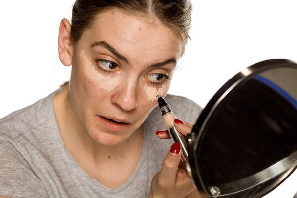 Young woman applying concealer on white background - Фото, зображення