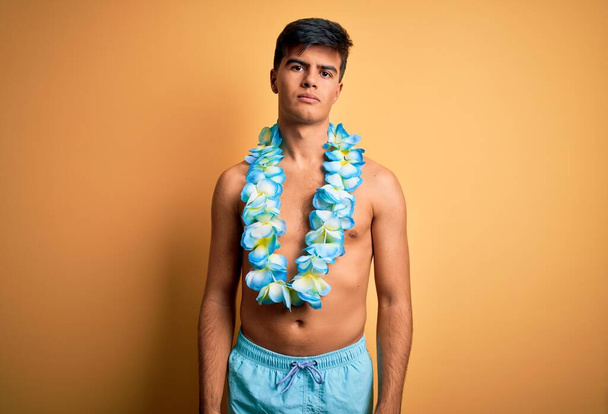 Junger gutaussehender Touristenmann in Badebekleidung und hawaiianischen Lei-Blumen entspannt mit ernstem Gesichtsausdruck. Einfaches und natürliches Betrachten der Kamera. - Foto, Bild