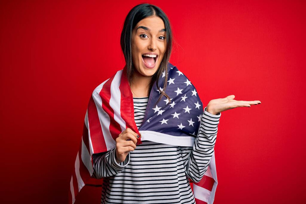 Joven hermosa morena patriótica mujer con bandera de los Estados Unidos para el día de la independencia muy feliz y emocionado, la expresión ganadora celebrando la victoria gritando con una gran sonrisa y las manos levantadas
 - Foto, imagen
