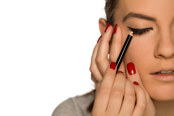 Mujer joven aplicando eyelinear sobre fondo blanco
 - Foto, Imagen