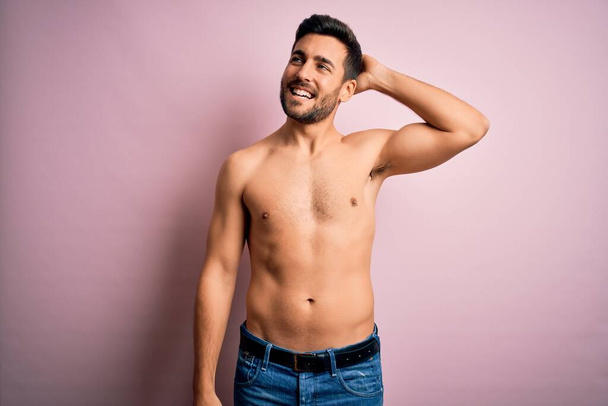 Νεαρός όμορφος δυνατός άντρας με γενειάδα χωρίς πουκάμισο στέκεται πάνω από απομονωμένο ροζ φόντο χαμογελώντας αυτοπεποίθηση αγγίζοντας τα μαλλιά με το χέρι προς τα πάνω χειρονομία, θέτοντας ελκυστική και μοντέρνα - Φωτογραφία, εικόνα