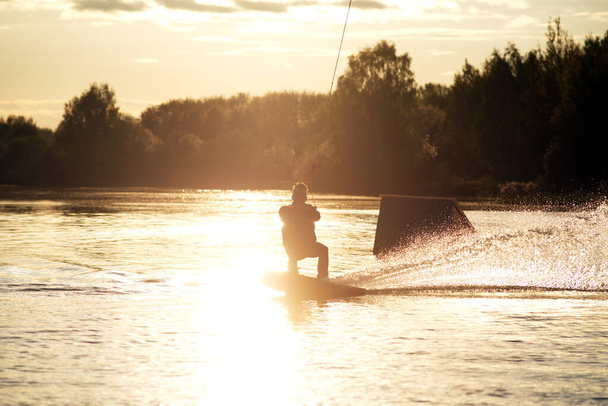 Wakeboarder haciendo trucos. Bajo ángulo de tiro del hombre wakeboarding en un lago
. - Foto, Imagen