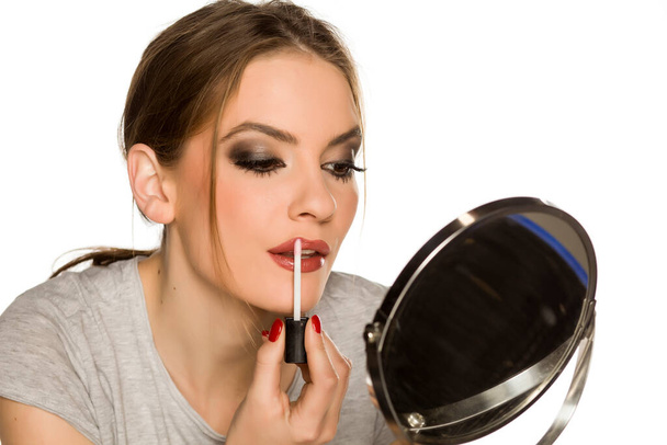 Nuori nainen soveltamalla huulikiiltoa valkoisella taustalla - Valokuva, kuva