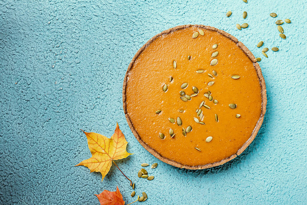 Fresh round bright orange homemade pumpkin pie on turquoise background, top view with copy space - Zdjęcie, obraz