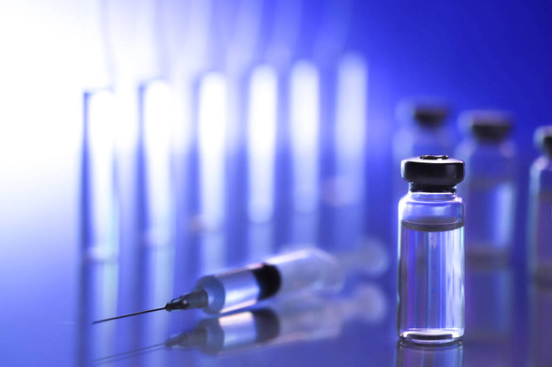 ampoule, glass vials and a medical syringe with a coronavirus vaccine on a blue background - Foto, afbeelding
