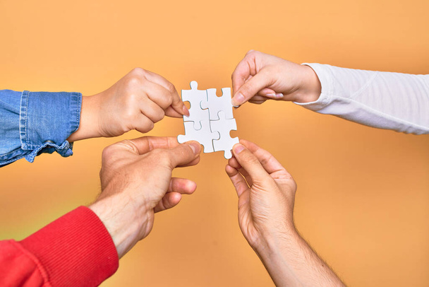 Hands of caucasian young people connecting pieces of puzzle over isolated yellow background - Foto, Imagem