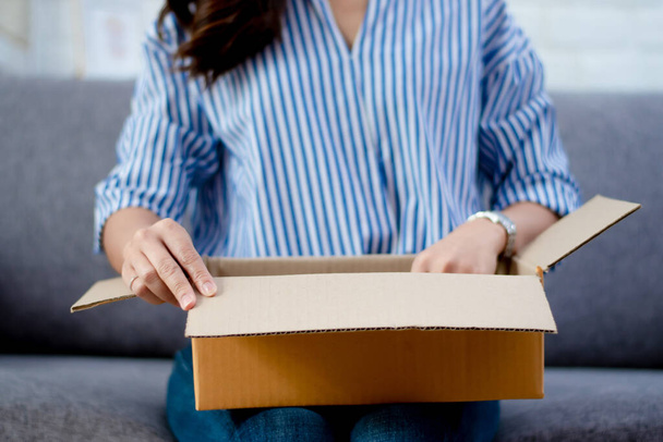 Primer plano de la mano de una mujer abriendo un paquete de cajas de cartón. Ella se sentó en el sofá en casa
. - Foto, Imagen