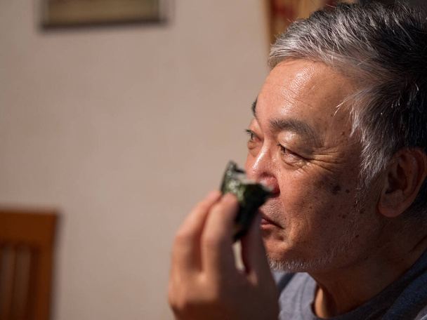An older man enjoying an onigiri rice ball in his home - Fotoğraf, Görsel