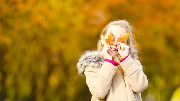 Retrato de adorable niña al aire libre en hermoso día cálido con hoja amarilla en otoño - Imágenes, Vídeo