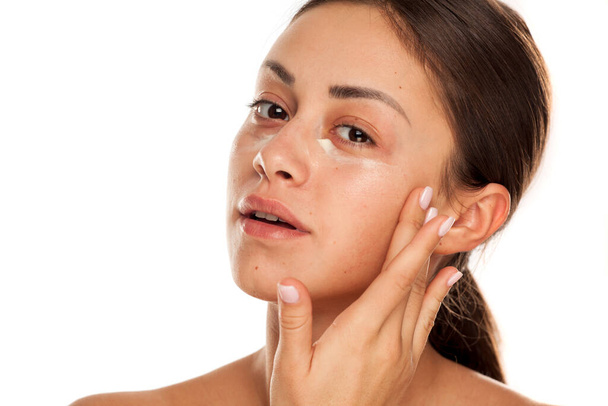 mooie jonge vrouw aanbrengen moisturizer op haar gezicht op witte achtergrond - Foto, afbeelding
