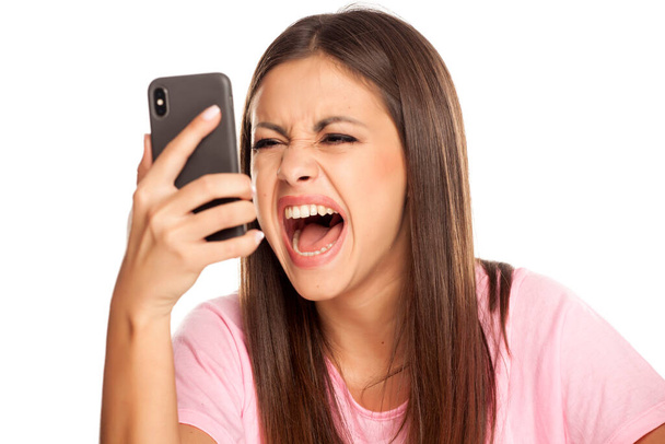 boze jonge vrouw screem in haar smartphone op witte achtergrond - Foto, afbeelding