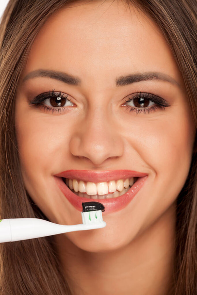 young woman holding electric tooth brush with black active charcoal toothpaste on white background - Фото, зображення