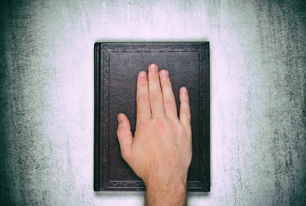 Uma palma masculina em um livro, um juramento sobre a Bíblia, vista superior de perto
 - Foto, Imagem