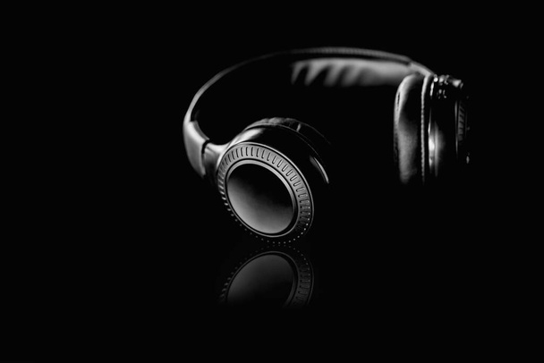 Auriculares inalámbricos negros sobre un fondo negro estilo de tono oscuro. - Foto, Imagen
