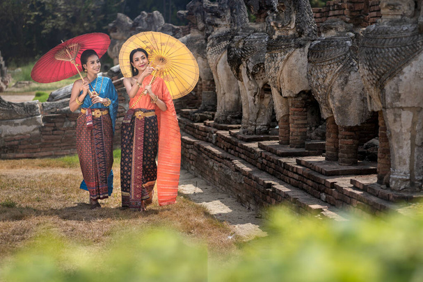Asian Thai women walking with umbrella in front of the Reclining Buddha, Pretty girl wearing in Thai dress costume traditional according Thai culture at Ayutthaya, Thailand - Photo, image