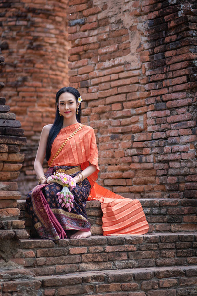 Pretty Asian women with beautiful garland in here hand and wearing traditional Thai dress costume according Thai culture at the ancient temple Ayutthaya, Thailand - Photo, image