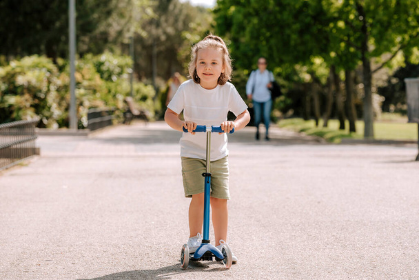 Хлопчик навчиться їздити на скутері в парку в сонячний літній день. Хлопчик дошкільного віку катається на роликах. Діти грають на відкритому повітрі з скутерами. Активний відпочинок та спорт на відкритому повітрі для дитини
. - Фото, зображення