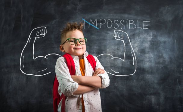 Change impossible on possible. Funny kid with strong arms against blackboard - Photo, Image