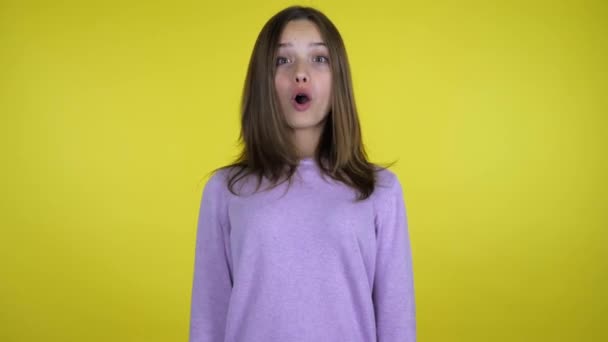 Teenager girl in a pink sweater is shocked on yellow background with copy space - Záběry, video