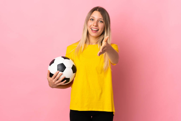 Young football player woman isolated on pink background handshaking after good deal - Foto, Imagen