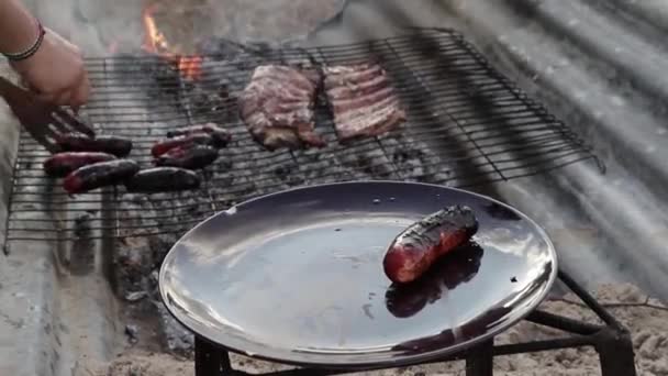 Una mano de un chico poniendo chorizos cocinados en la parrilla sobre un plato. A boy's hand putting cooked sausages on the grill on a plate. - Footage, Video