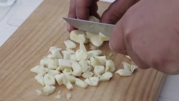 Una mano de un chico cortando dientes de ajo sobre una tabla de madera con un cuchillo. A boy's hand cutting garlic cloves on a wooden board with a knife. - Footage, Video