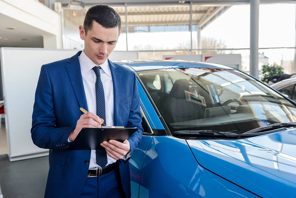 Businessman fills in documents on car at car dealership - 写真・画像