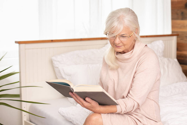 Старша жінка читає, зосереджена в книзі. Відпустка додому. Час дозвілля
. - Фото, зображення