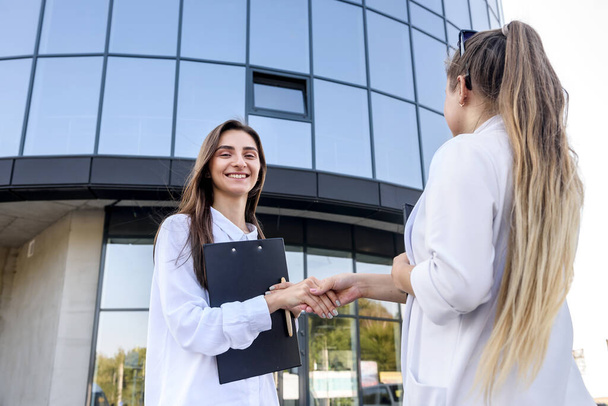 Business partners handshaking before office building. Two beautiful women in business suits smiling each other - Photo, Image