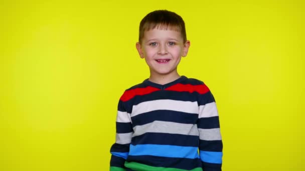 Cheerful little child boy smiles and looks at the camera on a yellow background - Footage, Video
