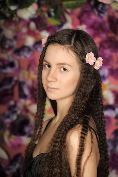 girl teenager brunette portrait with roses in hairstyle on a floral background - Fotó, kép