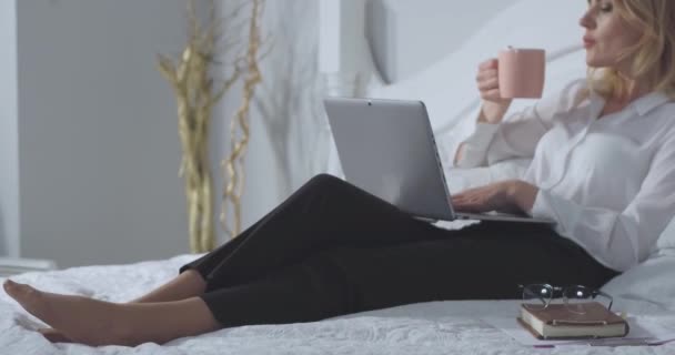 Businesswoman working on laptop enjoys a cup of hot coffee or tea before while working late night getting work done. Business woman relaxes in bed after a long flight. Business concept. Prores 422 - Filmmaterial, Video