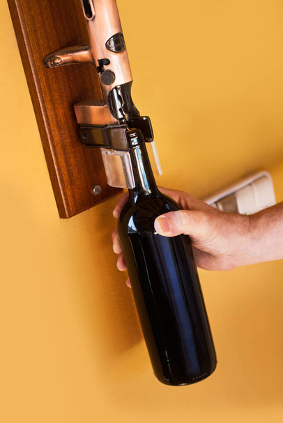 Man opening a bottle of red wine with a big metal corkscrew on a yellow wall - Foto, immagini