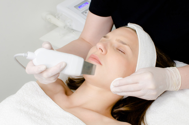 Kozmetológus, kozmetikus fehér kesztyűben, hogy arckezelés ultrahangos spatula fiatal nő, arc bőrtisztító kezelés ultrahangos spatula, arc tisztító eljárás szépségszalonban - Fotó, kép