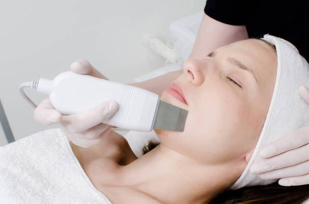 Cosmetólogo, esteticista en guantes blancos haciendo tratamiento facial con espátula ultrasónica para mujer joven, tratamiento de lavado de la piel de la cara con espátula ultrasónica, procedimiento de limpieza facial en salón de belleza
 - Foto, imagen